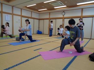 みんなで子どもをひざにのせてヨガのポーズをしている写真です