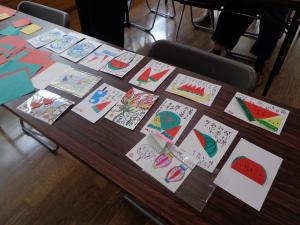 机の上に絵手紙の作品がたくさん並んでいる写真です。
